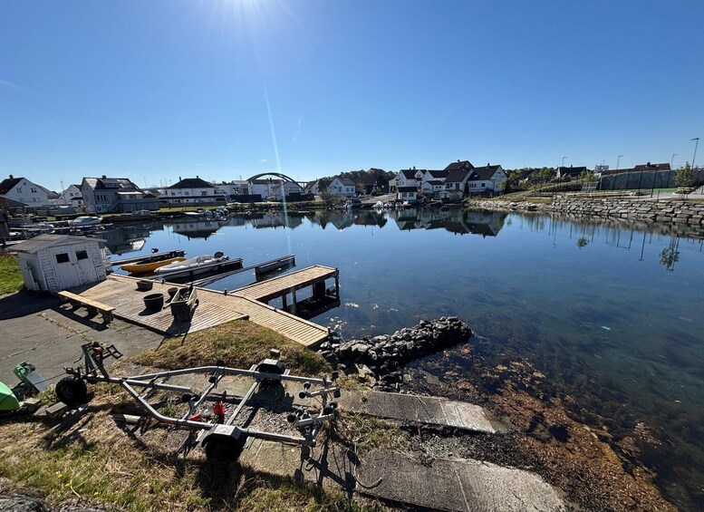 A calm harbor with boats, a dock, and houses in the background. 1