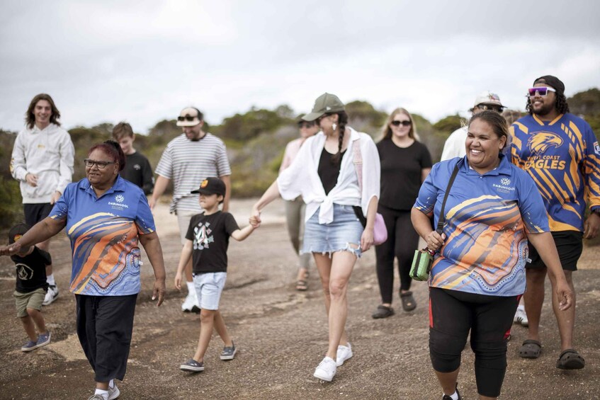 A group of people walking outdoors, some holding hands, with a dirt path and greenery in the background. 4