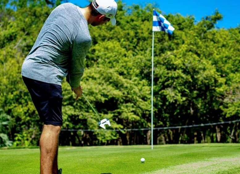 A person in a grey shirt and dark shorts preparing to put a golf ball on a green. 1