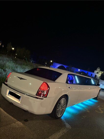 A white car with blue underglow lights parked in a lot at night. 3