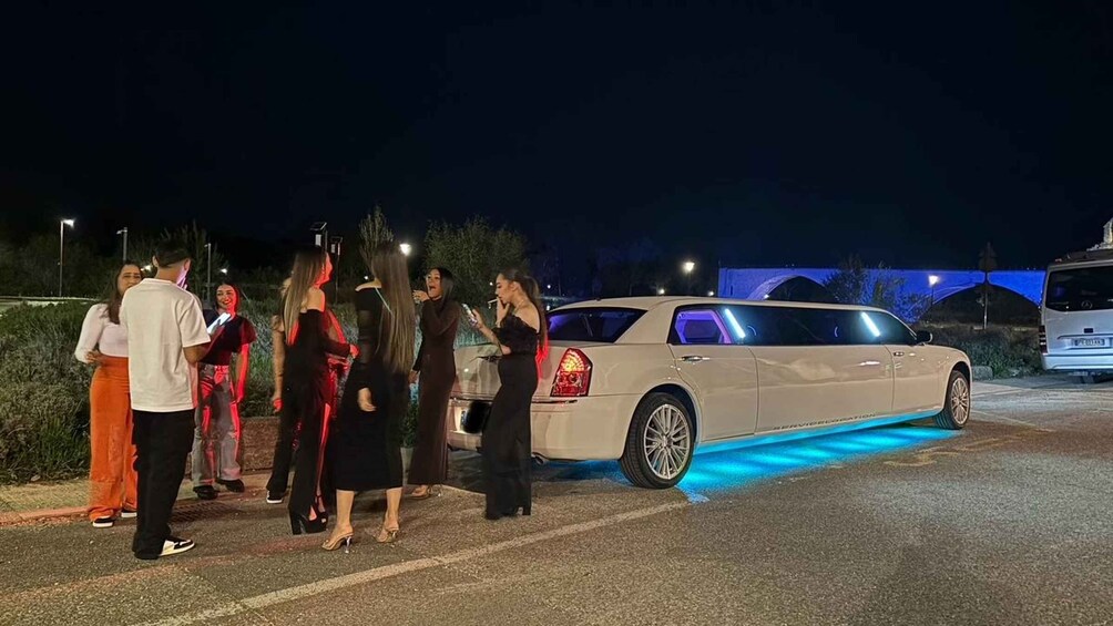 A group of people standing by a luxury car with blue underglow lights. 2