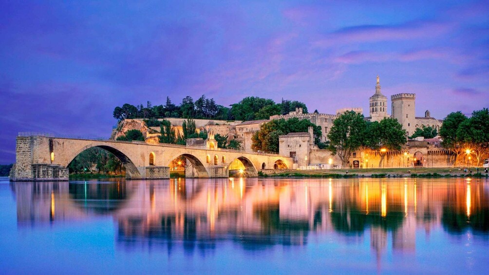 A historic stone bridge over a calm river, reflecting the surrounding architecture and trees. 4