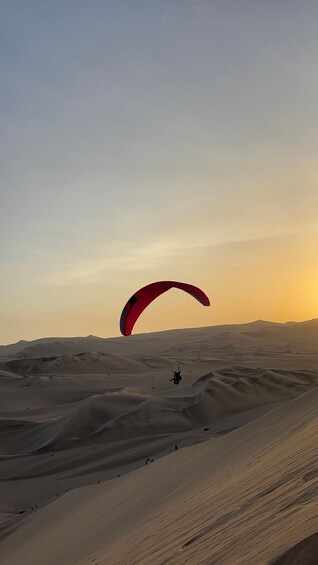 A person paragliding over a desert landscape with sand dunes. 1