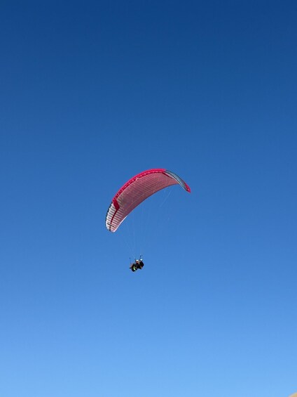 A paraglider with a red and white parachute against a clear blue sky. 3