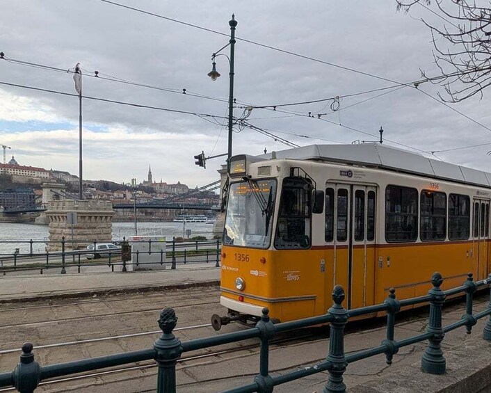A yellow tram numbered 1356 on tracks near a waterfront with buildings and a statue in the background. 5