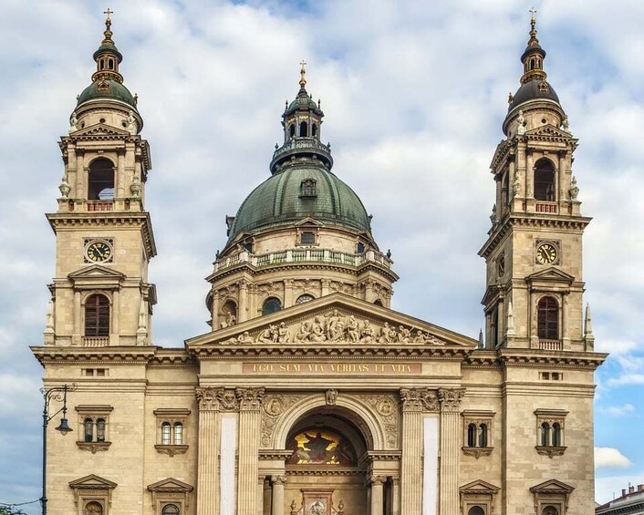 A historic building with a central dome, two towers with clocks, and an ornate entrance. 1