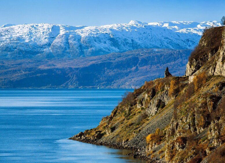 A snow-covered mountain range, a rocky coastline, and a calm body of water. 4