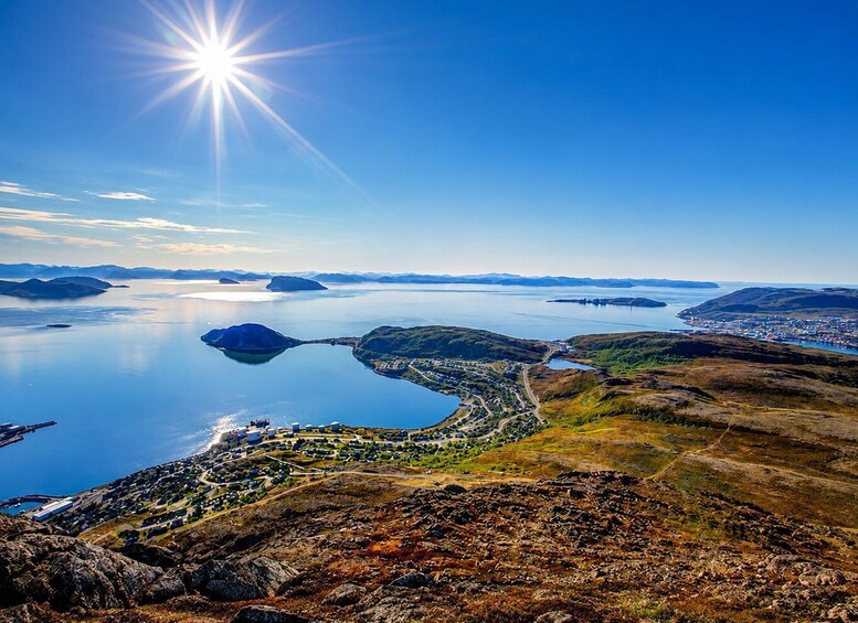 A coastal landscape with a clear sky, a large body of water, and a town nestled among hills. 5