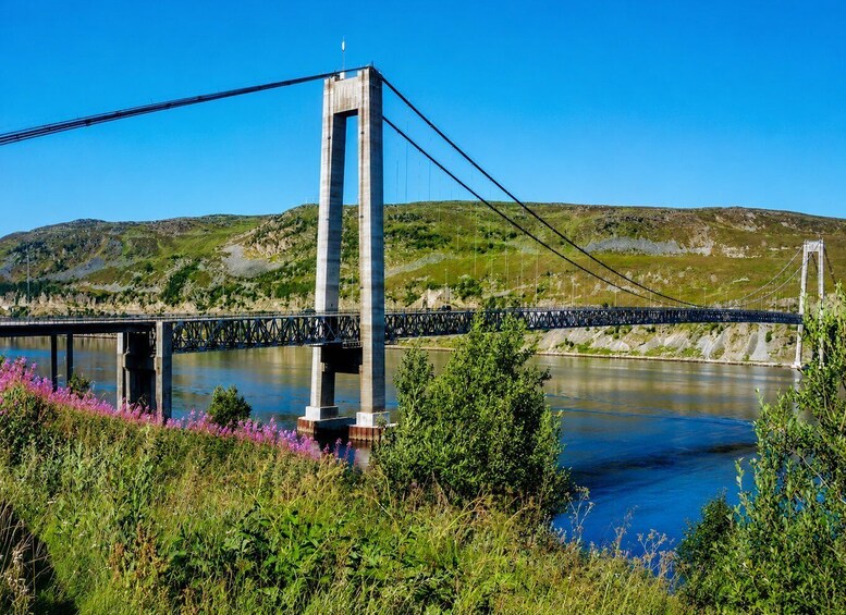 A suspension bridge over a river with hills in the background. 1