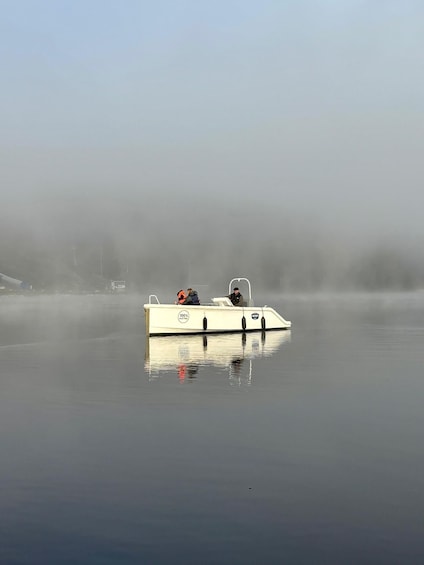 A white boat with '100% ELECTRIC' and 'LAPTOP' on its side, floating on calm water with a foggy background. 3
