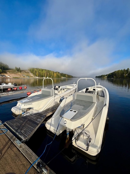 A calm lake with boats docked at a wooden pier, surrounded by trees and a cloudy sky. 1