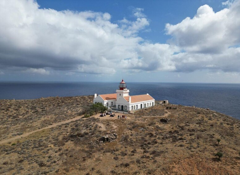 A white lighthouse with a red top on a hill overlooking the ocean. 1