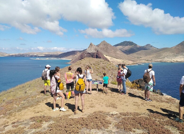 A group of people standing on a rocky cliff overlooking a coastal landscape with mountains in the background. 2