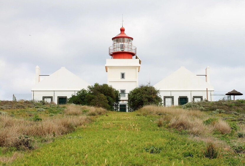A lighthouse with a red top, white base, and a white building with a green door in front. 4