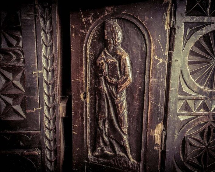 A weathered wooden door with a carved figure, geometric patterns, and a circular design. 5