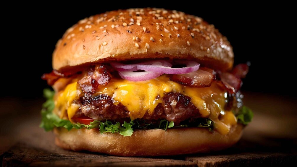 A close-up of a cheeseburger with lettuce, tomato, bacon, and red onion on a sesame seed bun. 5