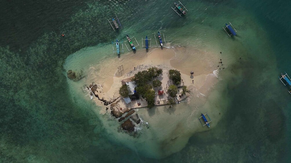 An aerial view of a tropical island with clear turquoise waters, a sandy beach, and several boats anchored near the shore. 2