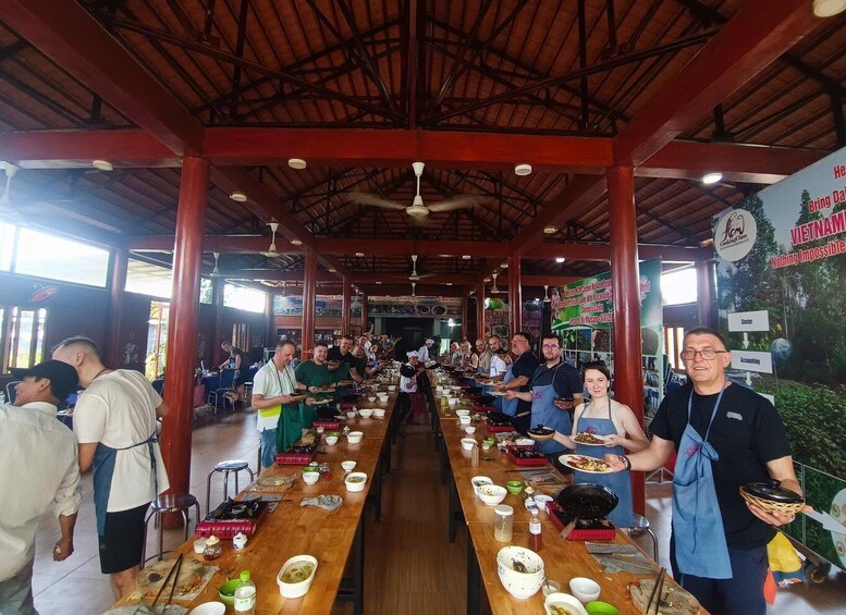 A long communal dining table in a restaurant with people seated and standing around it. 2