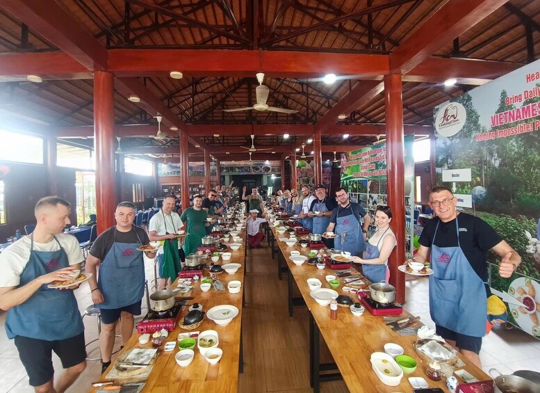 A group of people in a cooking class setting with a long table filled with cooking utensils and ingredients. 4
