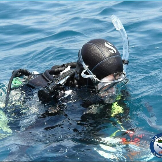 A diver in a black wetsuit and helmet with a snorkel, swimming in clear blue water. 2