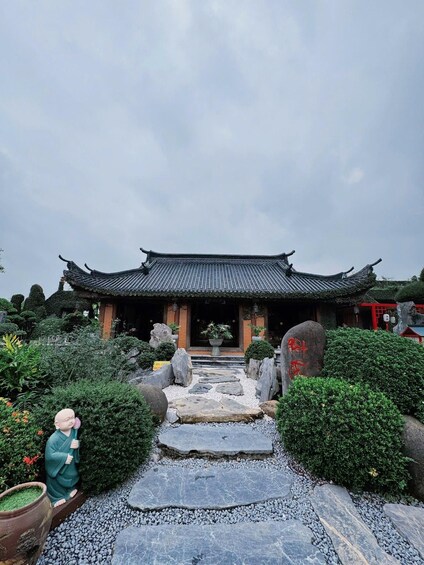 Un bâtiment traditionnel chinois, doté d’un toit en tuiles, entouré d’un jardin agrémenté de rochers, de plantes et d’une statue. 5