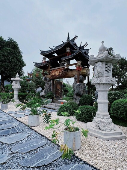 Un pavillon chinois traditionnel, doté d’une structure de toit complexe, entour é de lanternes en pierre et de plantes en pot. 3