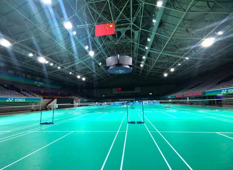 An indoor badminton court with a net, floodlights, and a Chinese flag. 1