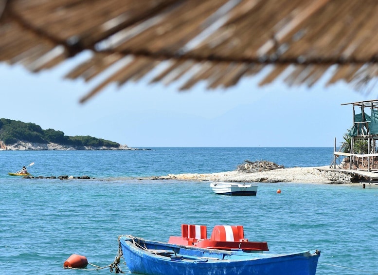 A calm sea with a blue boat anchored near the shore, a small boat on the rocks, and a beach with a wooden structure. 3