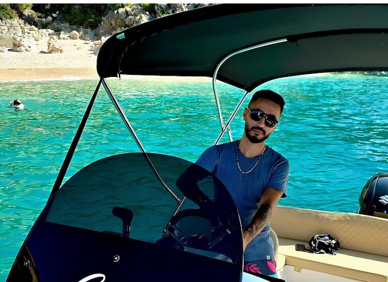 A person steering a boat with a beach and rocky shoreline in the background. 4