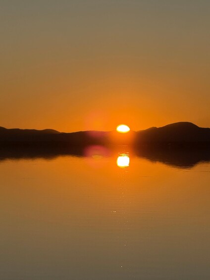 A sunset over a calm body of water with mountains silhouetted on either side. 3