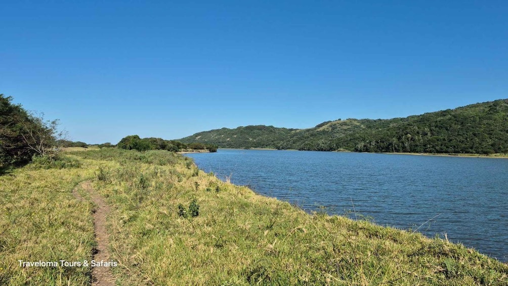 A river with a grassy path alongside, surrounded by hills and clear blue sky. 2