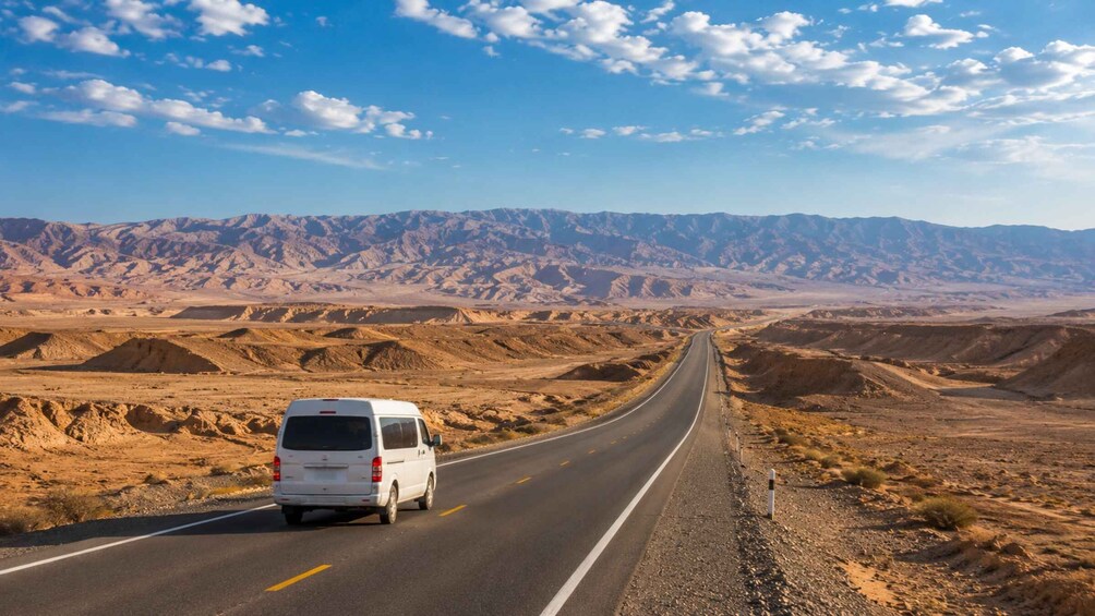A white van driving on a desert road with mountains in the background. 4