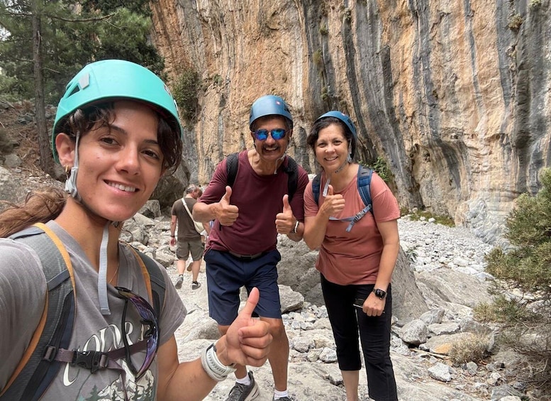 Three hikers giving thumbs up in a rocky canyon with steep cliffs. 1