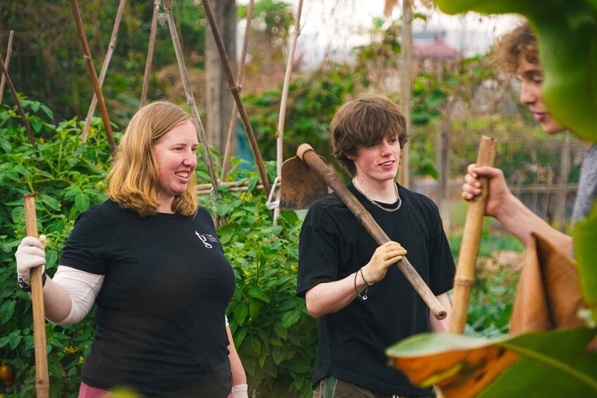 Three individuals in a garden holding gardening tools. 2