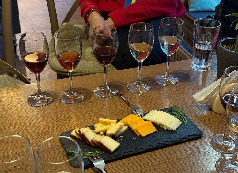 A wooden table with a cheese board, wine glasses, and a person in a red sweater. 3
