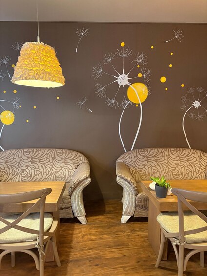 A cozy interior with patterned sofas, wooden chairs, a hanging light fixture, and a wall mural with abstract designs. 2