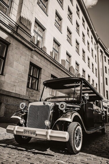 A vintage car parked in front of a building with a stone facade and multiple windows. 4