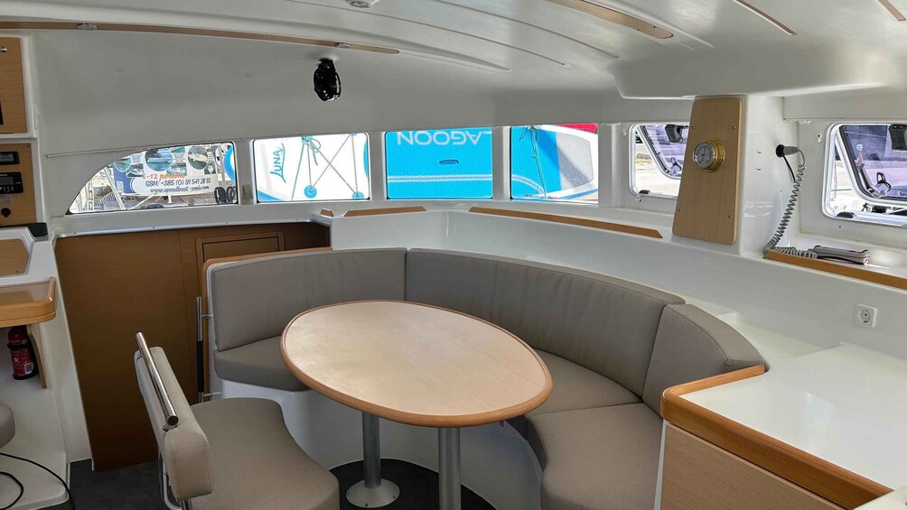A boat interior with a central table, cushioned seating, and windows displaying a marina scene. 5