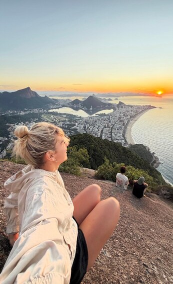 A person sitting on a cliff overlooking a cityscape with a sunset. 5