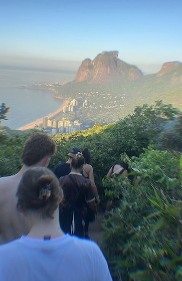 A group of people walking on a hillside with a city and mountains in the background. 2