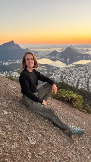 A person sitting on a rocky outcrop overlooking a cityscape with mountains in the background. 4