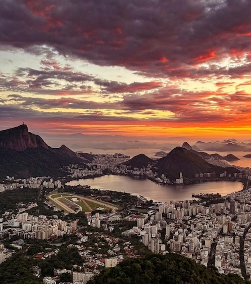 A cityscape with a large body of water, surrounded by mountains and a dramatic sunset sky. 1