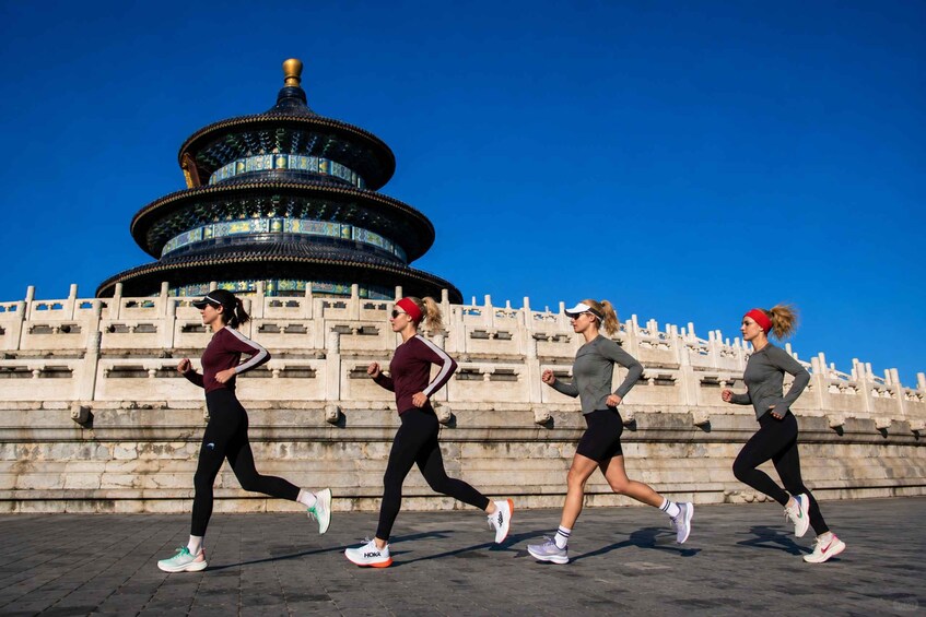 Four people running in front of a historical tower with a blue sky. 1