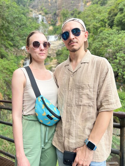 A couple standing on a bridge with a waterfall in the background. 5
