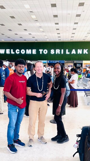 Three people standing in front of a 'WELCOME TO SRI LANKA' sign. 3