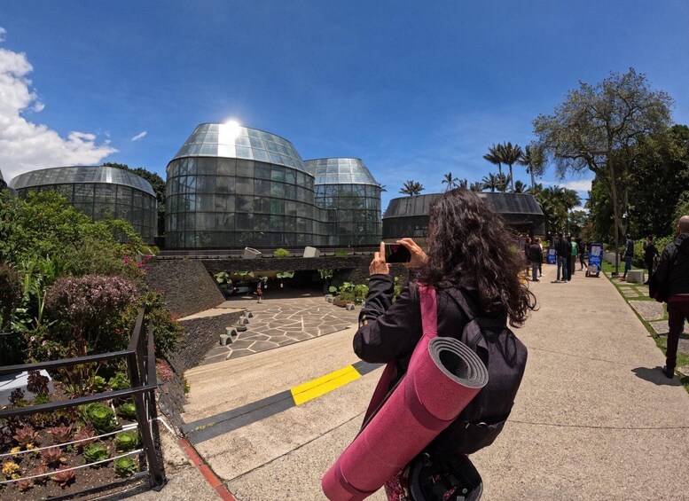 A person taking a photo of a modern glass building with a garden in the foreground. 1