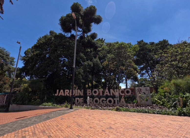 A sign for 'JARDIN BOTÁNICO DE BOGOTÁ' with a brick pathway and trees in the background. 3