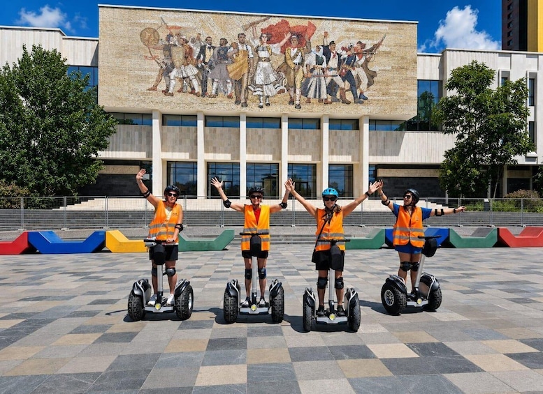 Four people on segways in front of a building with a large mural. 1