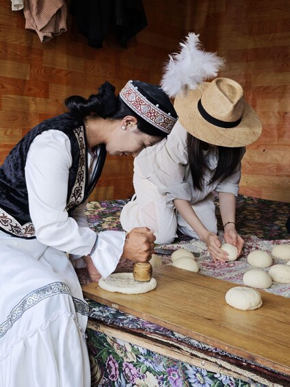 Two individuals kneading dough on a wooden surface with a patterned cloth. 1
