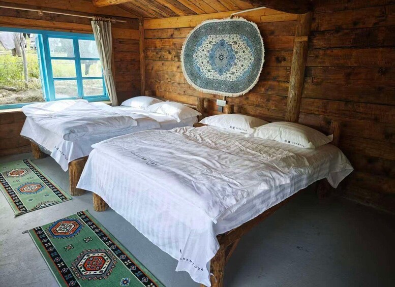 A wooden cabin with two beds, a blue window, and a patterned rug. 1
